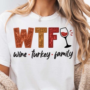 May include: White t-shirt with the text "WTF Wine - Turkey - Family" in red, orange, and yellow glitter lettering. A red wine glass with a red wine splash is next to the text.