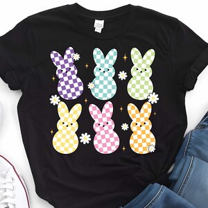 Puede incluir: Camiseta negra con un gr&aacute;fico de seis conejos con cuadros pastel con flores y estrellas blancas.