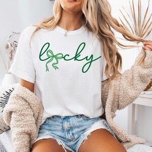 May include: White t-shirt with the word "lucky" written in green cursive with a green bow in the "c".
