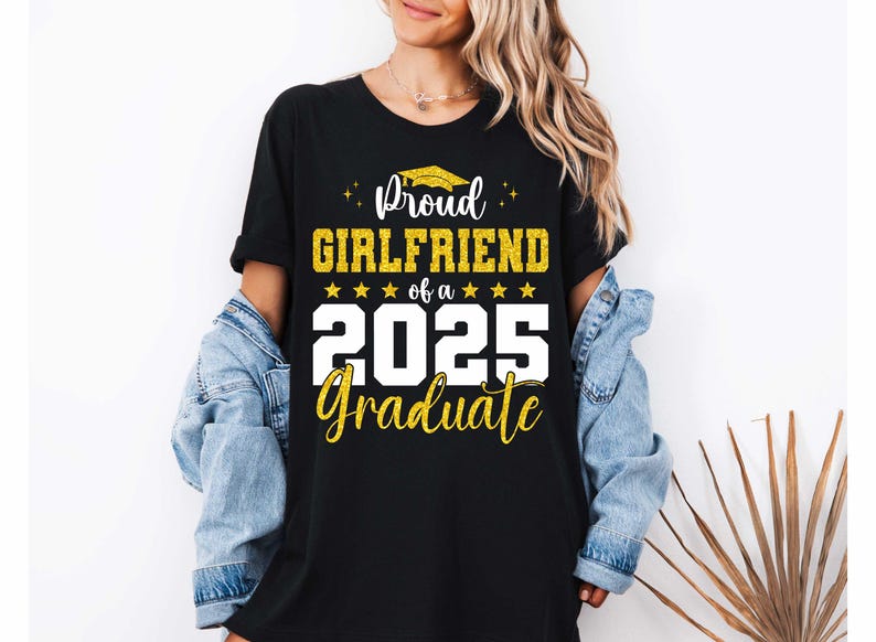 K&ouml;nnte beinhalten: Schwarzes T-Shirt mit wei&szlig;em Text, der "Proud Girlfriend of a 2025 Graduate" lautet. Der Text ist mit goldenem Glitzer und einer goldenen Abschluss-Kappe verziert.