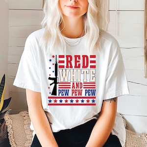 May include: White t-shirt with a red, white, and blue graphic design. The graphic features a stylized rifle with the words "RED WHITE AND PEW PEW PEW" and stars.