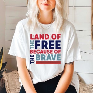 May include: White t-shirt with a red, white, and blue graphic that reads "Land of the Free Because of the Brave".