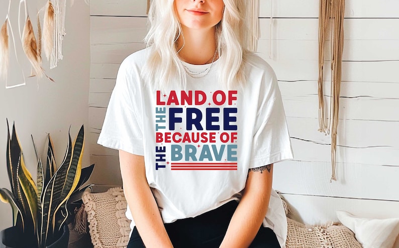 May include: White t-shirt with a red, white, and blue graphic that reads "Land of the Free Because of the Brave".