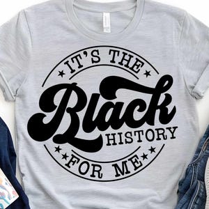 Puede incluir: Una camiseta gris con un diseño circular negro que dice "It's the Black History for Me" en una fuente retro.