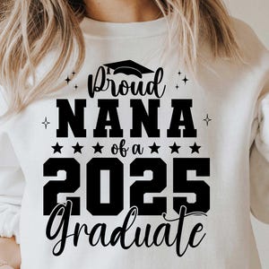 K&ouml;nnte beinhalten: Wei&szlig;er Pullover mit schwarzem Text, der "Proud Nana of a 2025 Graduate" lautet.
