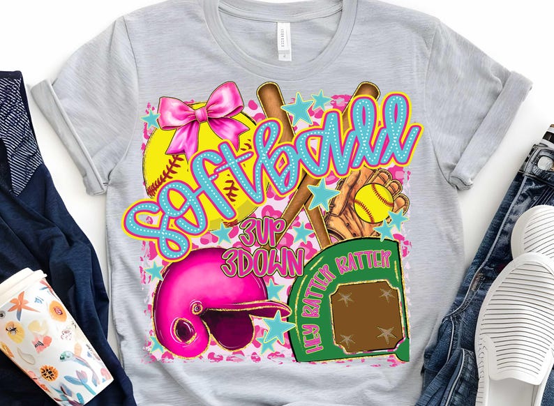 May include: A gray t-shirt with a pink, blue, and yellow softball design. The design includes a softball, bats, a glove, a helmet, and a home plate. The text "Softball" is written in blue and pink letters. The text "3 Up 3 Down" is written in black letters. The text "Hey Batter Batter" is written in green letters.