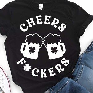 May include: Black t-shirt with white text that reads "Cheers F*ckers" and a graphic of two beer mugs with shamrocks.