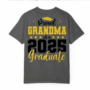 K&ouml;nnte beinhalten: Ein dunkelgraues T-Shirt mit goldfarbenem Glitzertext, auf dem "Proud Grandma of a 2025 Graduate" steht.