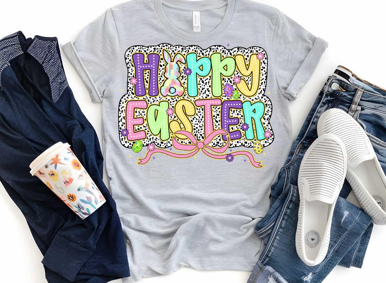 Puede incluir: Una camiseta gris claro con un gr&aacute;fico colorido de "Feliz Pascua" que presenta un conejito, flores y un lazo rosa. El gr&aacute;fico est&aacute; rodeado de un patr&oacute;n de lunares blanco y negro.