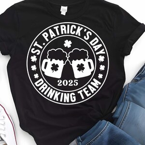May include: Black t-shirt with a white circle graphic that says "St. Patrick's Day Drinking Team 2025" with two beer mugs and shamrocks.