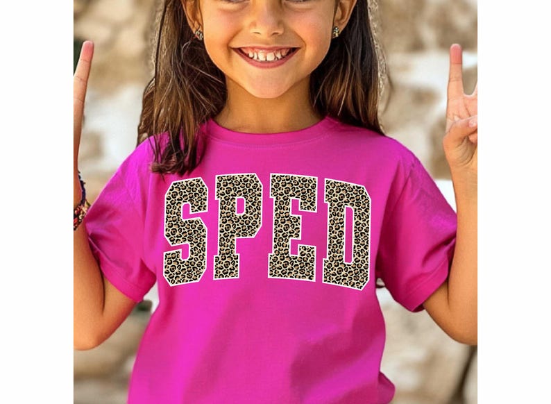 May include: A magenta t-shirt featuring the word "SPED" in large, bold letters. The letters have a leopard print pattern and white outlines. The shirt is worn by a young person.