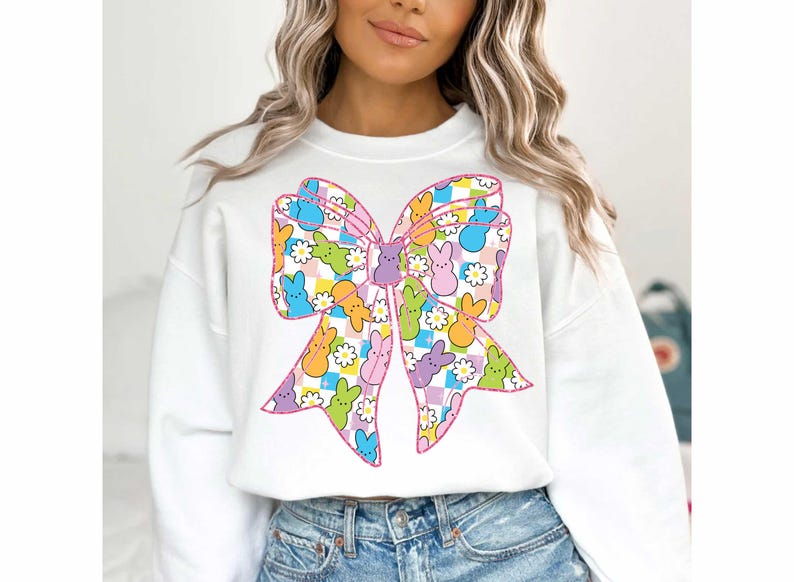 Puede incluir: Sudadera blanca con un dise&ntilde;o de lazo rosa. El lazo est&aacute; lleno de caramelos Peeps de colores.