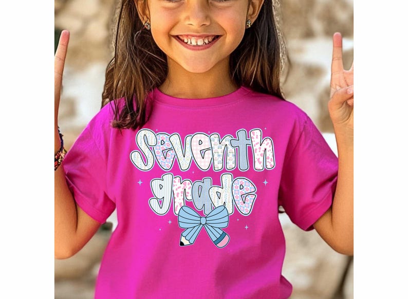 Pu&ograve; includere: Una maglietta rosa acceso con la scritta "Seventh Grade" in un font giocoso. Il design include un fiocco blu e una grafica a matita. Una scelta vivace per il ritorno a scuola o per l'uso quotidiano.