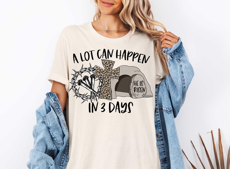 Puede incluir: Una camiseta blanca con un dise&ntilde;o gr&aacute;fico negro que dice "A lot can happen in 3 days". El gr&aacute;fico incluye una cruz con un dise&ntilde;o de estampado de leopardo, clavos, una corona de espinas y una tumba con las palabras "He is risen".