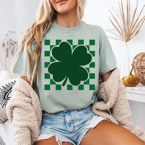 May include: A light green t-shirt with a green four-leaf clover graphic on a white and green checkered background.