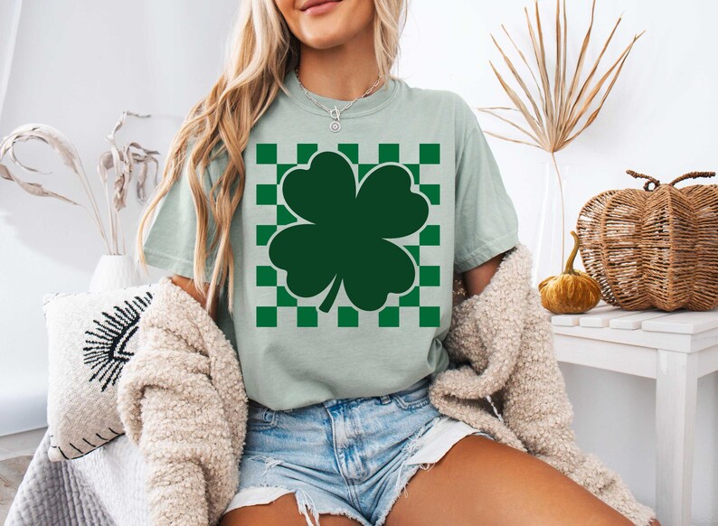 May include: A light green t-shirt with a green four-leaf clover graphic on a white and green checkered background.