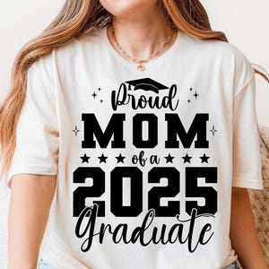 K&ouml;nnte beinhalten: Wei&szlig;es T-Shirt mit schwarzem Text, der "Proud Mom of a 2025 Graduate" lautet, mit einem Grafikbild eines Abschluss-Hutes &uuml;ber dem Wort "Proud".
