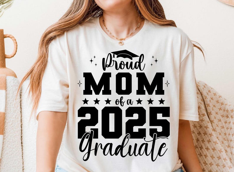 K&ouml;nnte beinhalten: Wei&szlig;es T-Shirt mit schwarzem Text, der "Proud Mom of a 2025 Graduate" lautet, mit einem Grafikbild eines Abschluss-Hutes &uuml;ber dem Wort "Proud".