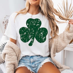 May include: A white t-shirt with a green shamrock design. The shamrock has a distressed look, giving it a vintage feel.