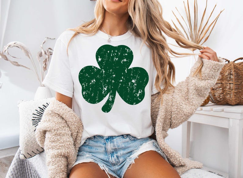 May include: A white t-shirt with a green shamrock design. The shamrock has a distressed look, giving it a vintage feel.