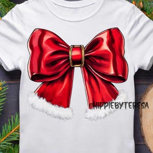 May include: White t-shirt featuring a large, glossy red bow with a gold-colored center. The bow has white faux fur trim at the bottom. The text "HIPPIEBYTERESA" is printed on the shirt. Festive apparel.