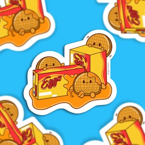 May include: A sticker featuring cartoon waffles and Eggo boxes on a blue background. The waffles have smiling faces and are surrounded by syrup. The Eggo boxes are yellow and red.