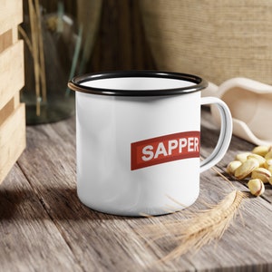 May include: White enamel mug with a black rim and handle. The mug has the word "SAPPER" printed in red on a red rectangle.