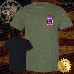 May include: Olive green t-shirt with a small emblem on the chest featuring a blue and red design and the words "10th Mountain Division" and "Fort Drum, New York." A black t-shirt is shown below. The shirt is available in long sleeve tee, hoodie, and sweatshirt.