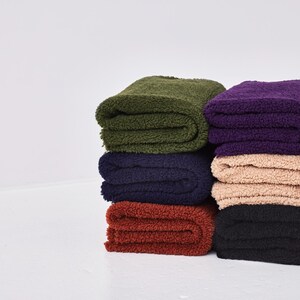 Puede incluir: Una pila de seis mantas de felpa dobladas en varios colores, incluyendo verde, morado, beige, negro y rojo. Las mantas son suaves y esponjosas, perfectas para acurrucarse en el sofá.