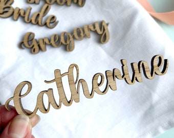 May include: Wooden name place cards with the names "Groom", "Bride", "Gregory", and "Catherine" written in cursive.