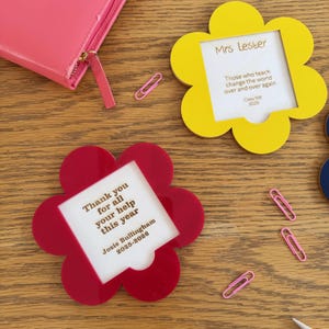 May include: Two flower-shaped frames, one yellow and one red, with text inserts. The yellow frame reads "Mrs Lester" and the red frame reads "Thank you for all your help this year." Pink paperclips and a pink wallet are also visible.