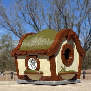 May include: A brown and white birdhouse with a green roof and a round opening for birds to enter. The birdhouse has a small window and two small planters on the front.
