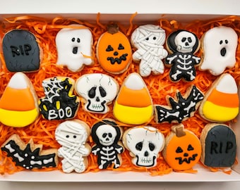 May include: A box filled with Halloween-themed sugar cookies. The cookies are decorated with various designs, including ghosts, pumpkins, candy corn, skeletons, and bats. The box is lined with orange shredded paper.