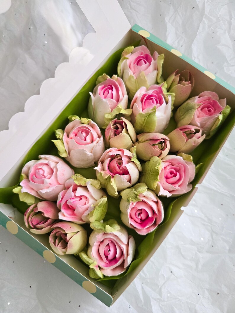 May include: A box of pink and white rose-shaped treats, possibly marshmallows or candies, arranged on green paper. The roses have a vibrant pink center and are nestled in a box with a polka dot design.