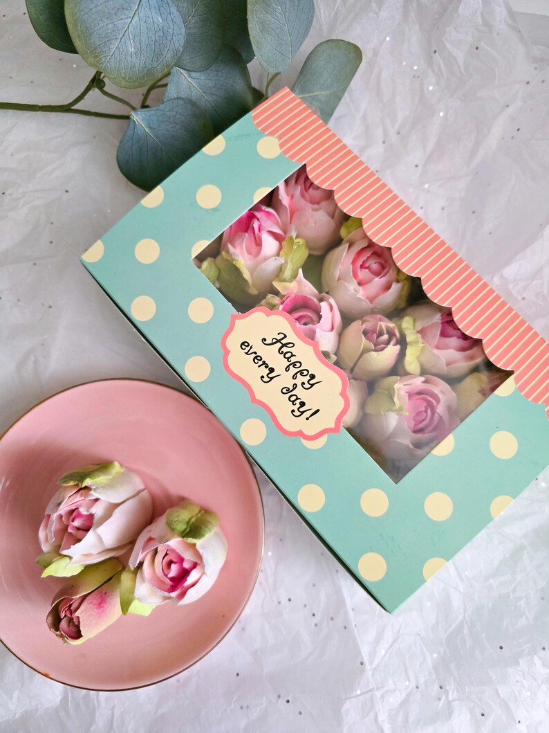 May include: A box of pink and white artificial roses with green leaves, displayed on a pink plate. The box is light blue with white polka dots and a pink scalloped edge. The box has a label that says "Happy every day!"