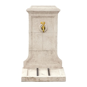 May include: A white stone fountain with a gold faucet and a small basin at the bottom.