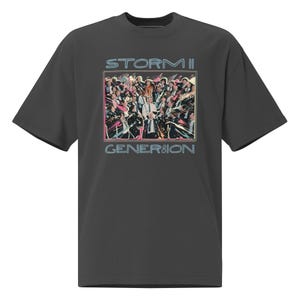 Puede incluir: Una camiseta de manga corta gris carbón con un gráfico rectangular central. El estampado muestra una multitud de personas con ropa formal, rayas de luz coloridas y el texto STORM II GENERATION en una fuente azul claro contorneada.