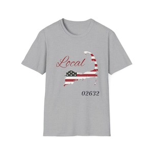 May include: A grey t-shirt with a graphic of a map outline in the style of the American flag. The word "Local" is written in a cursive font above the map, and the number "02632" is below it.