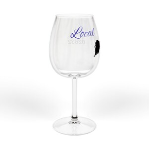 May include: A clear wine glass with a long stem and a round base. The glass has the word "Local" in blue script, the word "season" in a smaller font, and a black silhouette of a state. The glass is empty.
