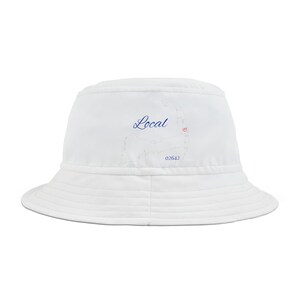 Pode incluir: Chapéu branco de pescador com um contorno bordado em azul de Cabo Cod e a palavra "Local" em escrita azul. O contorno inclui um pequeno coração vermelho. O número "02642" também está bordado em azul.