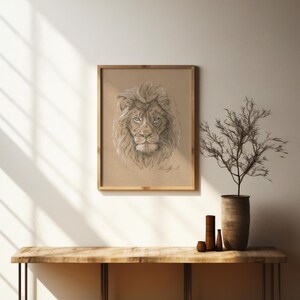 May include: A framed black and white pencil drawing of a lion's head with a serious expression. The drawing is on a light brown background and is framed in a natural wood frame.