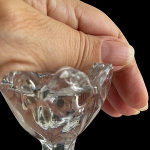 May include: A clear, cut-glass pedestal dish with a scalloped rim. The dish has a diamond pattern on the base and a faceted stem. The dish is held against a black background.