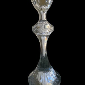 May include: A clear glass candlestick holder with a flared, scalloped top and a diamond-patterned midsection. The base is rounded, and the stem is slender, creating an elegant, decorative piece.
