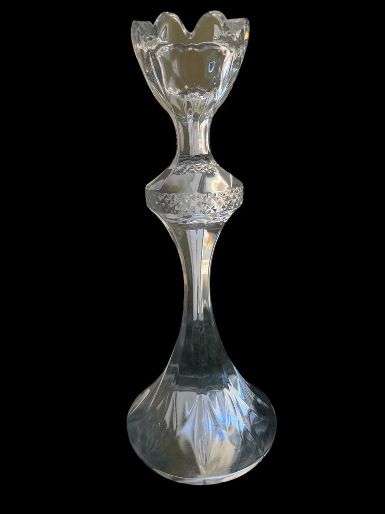 May include: A clear glass candlestick holder with a flared, scalloped top and a diamond-patterned midsection. The base is rounded, and the stem is slender, creating an elegant, decorative piece.