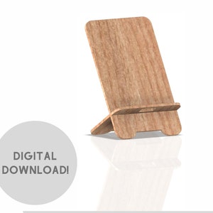 以下が含まれることがあります： 明るい木材仕上げの木製電話スタンド。スタンドは傾斜しており、電話を保持するための小さな棚があります。画像には「デジタルダウンロード！」というテキストと、DXF、SVG、CDR、PDFのファイルタイプアイコンが含まれています。