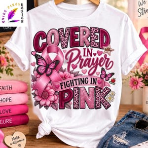 以下が含まれることがあります： COVERED IN PRAYER FIGHTING IN PINKという文字がデザインされた白い半袖Tシャツ。デザインには、大きなピンクの啓発リボン、蝶、花、小さなハート、カウボーイハット、ヒョウ柄のパターンが含まれています。