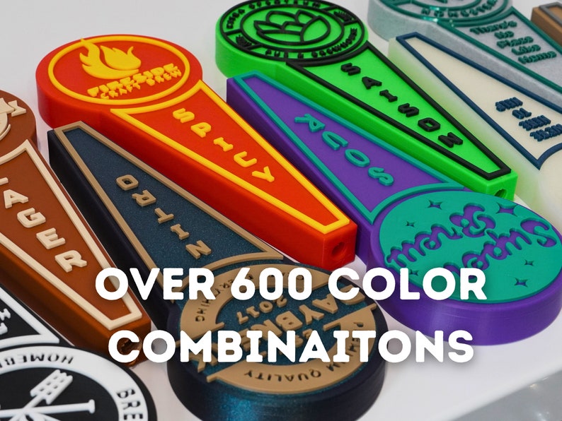 May include: A close-up of colorful, 3D printed beer tap handles with various designs and text, including "Fireside Craftworks", "Nitro", "Sails", "Across", "Mango Dreams", and "Lager". The text "OVER 600 COLOR COMBINATIONS" is displayed below the handles.