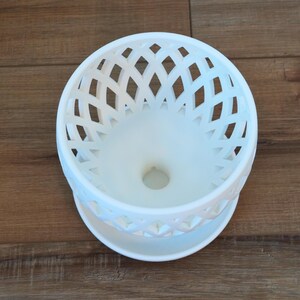 May include: White ceramic planter with a decorative lattice design. The planter has a drainage hole in the bottom.