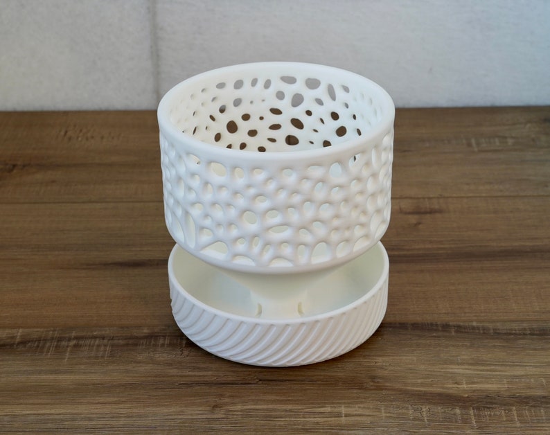 May include: White ceramic planter with a decorative, openwork design. The planter has a lower section with a textured, ribbed design.