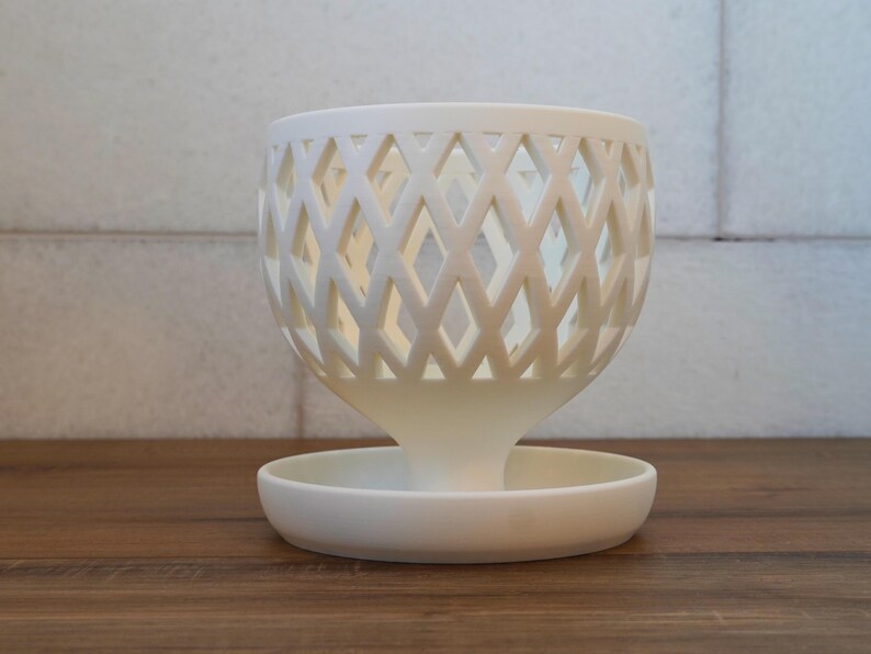May include: White ceramic planter with a diamond-shaped lattice design. The planter has a wide, shallow base and a narrow, cylindrical top.